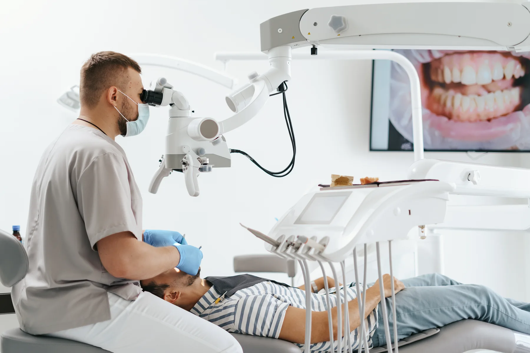 A dentist treating a patient beside a dental scan